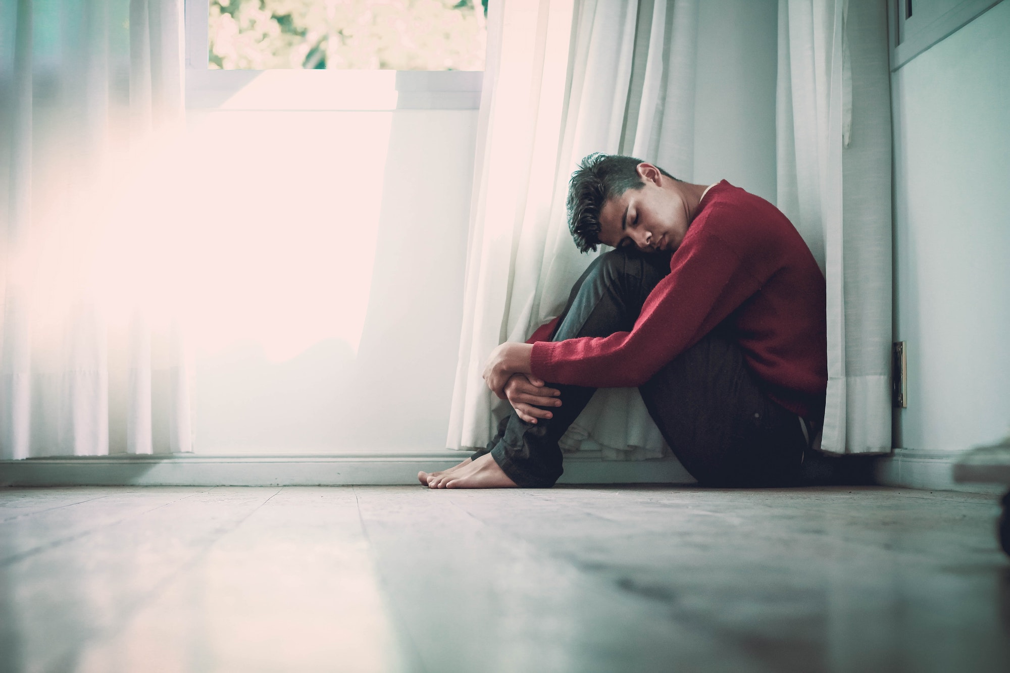 young man curling up in corner of room